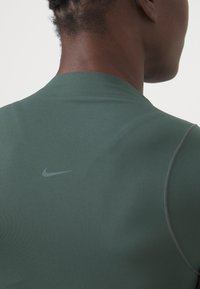 Grünes Sportshirt, figurbetontes Design, glatte Textur, mit einem dezenten grauen Nike-Logo auf der Rückseite in der Nähe des Halsausschnitts, mit flachen Nähten.