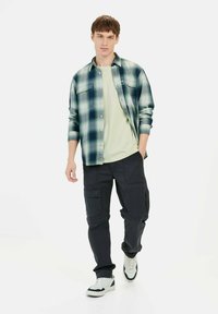 Flannel skjorte i blå og grøn rutet, lysegrøn t-shirt, sorte cargo bukser og hvide sneakers. Afslappet outfit der egner sig til forskellige anledninger.