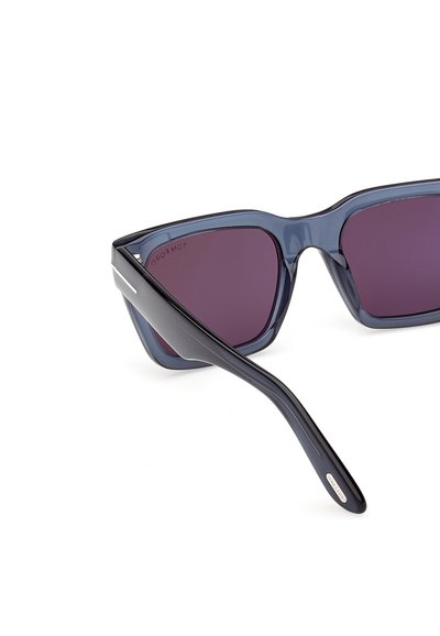 Detailní záběr tmavě průsvitných modrých kočičích brýlí s fialovými čočkami a černými stranicemi na bílém pozadí.