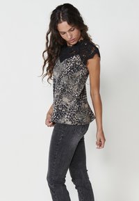 Top con stampa leopardata e maniche a cappuccio in pizzo nero, caratterizzato da un design fluido e una texture morbida, abbinato a jeans neri aderenti.