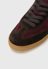 Zapatillas de ante en marrón oscuro y burdeos, con cordones redondos, puntera reforzada y suela de goma texturizada.