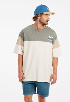T-shirt met korte mouwen in groen, beige en crème kleurvlakken, met een golflogo. Draag het met blauwe shorts en een blauwe pet.