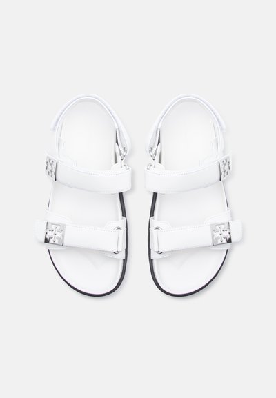 Λευκά σανδάλια με δύο ρυθμιζόμενα λουράκια που διαθέτουν ασημένιες αγκράφες με λογότυπο, ανοιχτά δάχτυλα και μαύρα άκρα σόλας, εμφανιζόμενα από πάνω σε λευκό φόντο.