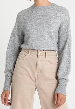 Light gray knit sweater featuring a ribbed crew neckline and loose sleeves, paired with high-waisted beige corduroy pants.