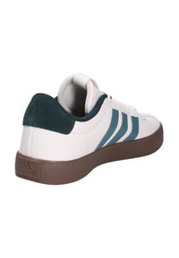 Zapatilla blanca con rayas en color teal, talón de ante y suela de goma marrón. Presenta un upper de cuero texturizado y un cuello acolchado para mayor comodidad.
