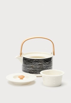 Théière en céramique avec motif à pois noirs, poignée en bois, couvercle blanc avec bouton en bois et infuseur perforé sur fond blanc.