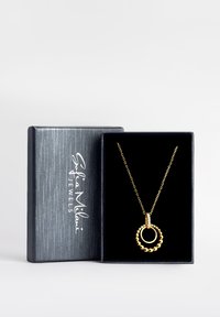 Guld vedhængs halskæde med cirkelformet design og en struktureret ydre ring, præsenteret i en gaveæske med sort fløjlsforing.