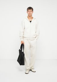 Felpa con zip bianca e pantaloni della tuta abbinati, abbinati a una borsa tote nera e scarpe da ginnastica bianche con dettagli neri. Texture del tessuto liscia.
