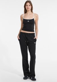 Black tank top with white trim and star detail, paired with black jogger pants featuring an elastic waistband and side pockets.