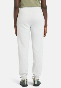 Pantalon de jogging gris clair avec une ceinture élastique, des poignets fuselés et une texture douce. Assorti à des chaussures de sport noires et vertes.