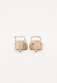Chaussures à talons en suède beige avec un design simple, une sangle à la cheville et un talon bloc étroit. La texture douce et la forme arrondie des orteils sont prédominantes.