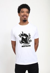 Hvid bomulds t-shirt med en sort grafisk tryk af en siddende figur, omgivet af plante-motiver, og teksten "MATISSE" nedenfor.