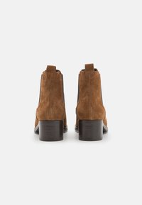 Botas ankle de ante marrón con un tacón bajo tipo bloque, que cuentan con paneles laterales elásticos y tiradores para un fácil uso. Diseño suave y limpio.