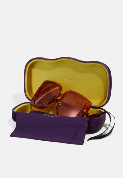 Gucci prillid oranžis raamis, toonitud objektiividega, asetatud lillasse karpi, mille sees on kollane vooder ja sellele sobiv lillakas kott.
