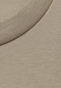 Tessuto di cotone in una tonalità beige con un colletto a coste testurizzato. Superficie liscia con un modello di maglia coerente, che enfatizza morbidezza e flessibilità.