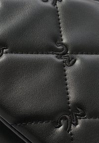 Materiale in pelle nera con sezioni imbottite, cuciture visibili e dettagli in rilievo. Superficie testurizzata con una finitura liscia.