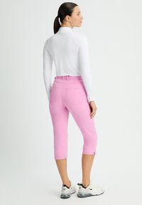 Lätt vit långärmad topp som är ihop med rosa knälånga byxor med bakfickor och sprund vid fållen, bärs med vita sneakers.