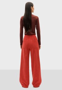 Pantaloni larghi rossi con un'alta vita elasticizzata, realizzati in tessuto testurizzato, con tasche posteriori e una vestibilità leggermente ampia.