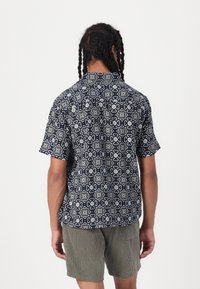 Chemise à col et à manches courtes de couleur bleu foncé avec un motif floral blanc. La vue arrière montre une coupe décontractée et une texture de tissu lisse.