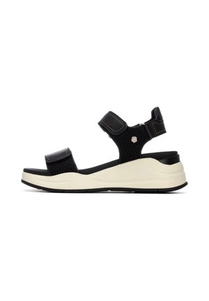 Sandalia de malla negra con correas ajustables, entresuela blanca y suela de goma. Presenta un diseño elegante con costuras contrastantes y un detalle de logo.