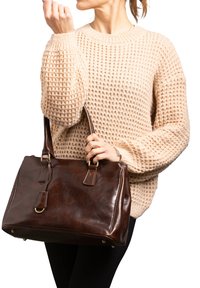 Bruine leren handtas met een gestructureerde vorm, twee handvatten, gouden hardware en een gladde, glanzende textuur. Draag het met een beige gebreide trui.