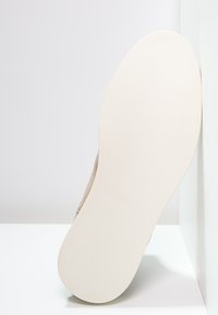 Sole béžové boty s hladkou, plochou světlou gumovou podrážkou směřující k divákovi na bílém pozadí.