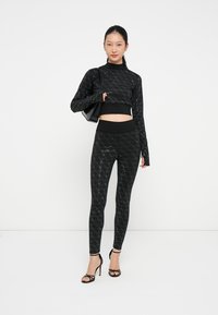 Crop top nero a maniche lunghe e leggings abbinati con un motivo a diamante testurizzato, abbinati a tacchi a spillo neri e una piccola borsa.