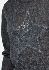 Top grigio lavorato a maglia con un design a stella in paillettes argentate, dalla texture morbida e un aspetto leggermente trasparente.
