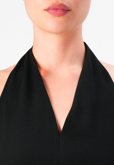 Close-up of a woman’s lower face, neck, and upper chest wearing a black halter top with natural skin tone and red lipstick.