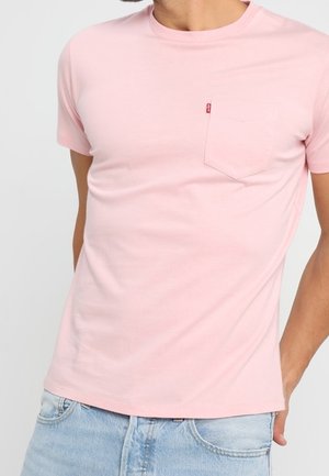 T-shirt en coton rose clair avec col rond et manches courtes, doté d'une petite poche poitrine et d'un détail d'étiquette rouge.