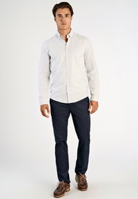 Πουκάμισο με κουμπιά σε ανοιχτό ριγέ ύφασμα, συνδυασμένο με σκούρο μπλε παντελόνι και καφέ παπούτσια. Το πουκάμισο έχει γιακά και καμπυλωτό τελείωμα.