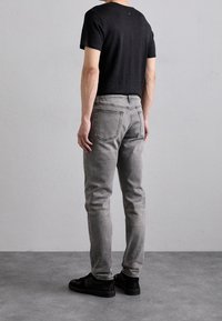 Jeans in denim grigio con una vestibilità slim e un leggero sbiadimento, abbinati a una maglietta nera a maniche corte. Sneakers nere completano l'outfit.