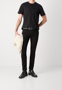 Czarny bawełniany T-shirt z krótkim rękawem, czarne dżinsy i czarne skórzane buty. Trzyma jasny płaszcz. Okrągły dekolt, minimalna metka.