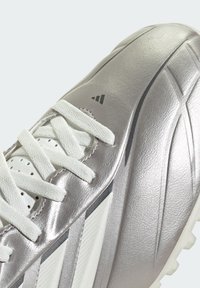 Baskets argentées avec lacets blancs, tige texturée, languette perforée et bandes sombres en relief sur le côté.