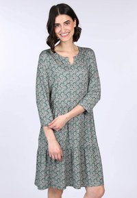 Blumenmuster-Kleid aus grünem Stoff mit einem gestuften Design, V-Ausschnitt und Dreiviertelärmeln, das mit einem zarten Blumenmuster durchzogen ist.
