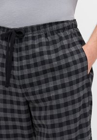 Pantalon de lounge noir et gris à carreaux avec une taille élastique, fermeture à cordon de serrage et poches latérales. Le matériau est léger et doux.