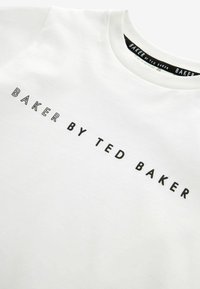 Valkoinen puuvillatee paita, jossa teksti "BAKER BY TED BAKER" mustalla, klassisella pyöreällä kaula-aukolla ja sileällä pinnalla.