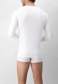 Camicia bianca a maniche lunghe realizzata in materiale morbido, design aderente, texture liscia, con pantaloni corti bianchi coordinati. Aspetto semplice e senza cuciture.