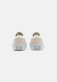 Zapatillas de lona blanca y ante beige con suelas de goma gris, que presentan un logo de Vans en el talón y un diseño simple y estilizado.
