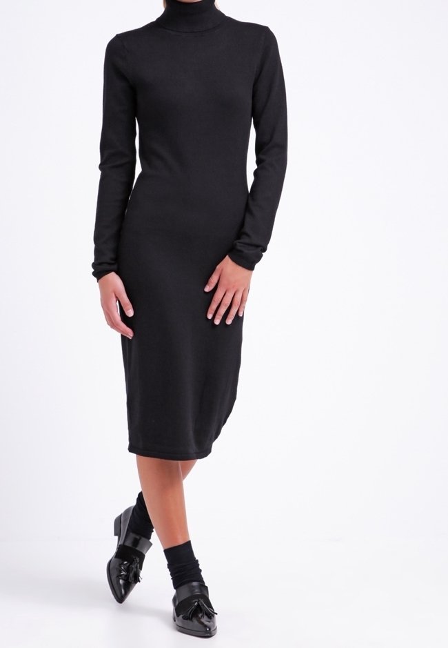 Svart polotröja klänning, knä-lång, figurnära silhuett, ribbad textur, långa ärmar. Matchad med svarta skor med dekorativ accent.