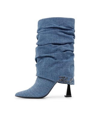 Mid-calf slouchy boot made of blue denim with pointed toe, black geometric heel, and metal "Karl" logo near heel.