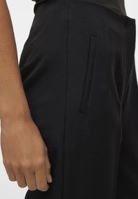 Svarta skräddarsydda byxor med en jämn textur, med en sidoficka med en stilren öppning och en åtsittande silhuett.