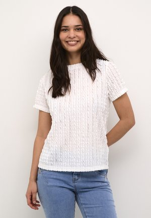 Bílá blůza s krátkým rukávem, texturovaným, plisovaným designem, kulatým výstřihem a ohrnutými manžetami, v kombinaci se světle modrými džíny.
