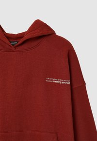 Sweat à capuche bordeaux avec une poche kangourou, doté d'un imprimé texte graphique à l'avant. Fabriqué en coton doux, il offre une coupe décontractée et une capuche ajustable.