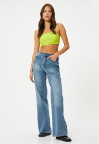 Top corto verde y jeans de mezclilla de pierna ancha de color azul claro, con cintura alta, un desvanecimiento sutil y un ajuste relajado. Zapatos negros completan el conjunto.