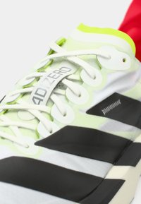 Vihreä ja valkoinen juoksukenkä, jossa on synteettinen päällinen, mustia yksityiskohtia, teksturoitu pohja ja näkyvä ADIZERO-brändäys kielessä.