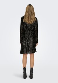 Rochie neagră brodată cu mărgele, cu mâneci lungi, talie strânsă și fustă amplă. O pereche de cizme negre până la gleznă cu toc pătrat completează ținuta.