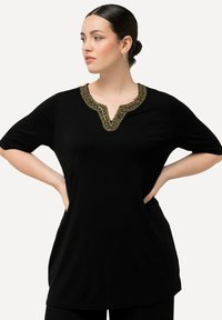 Tunic nera con scollatura a V impreziosita da perline colorate attorno al colletto. Tessuto leggero, maniche corte, vestibilità ampia.