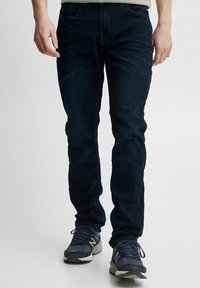 Tumedat sinised denim püksid, millel on kitsas lõige, viis taskut ja õrn fade efekt. Kantud tumesiniste spordijalatsitega, et saavutada juhuslik välimus.