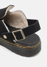 Crne suede sandale s debelim teksturiranim potplatom, udobnom unutarnjom oblogom, podesivom kopčom i detaljima od žute niti.